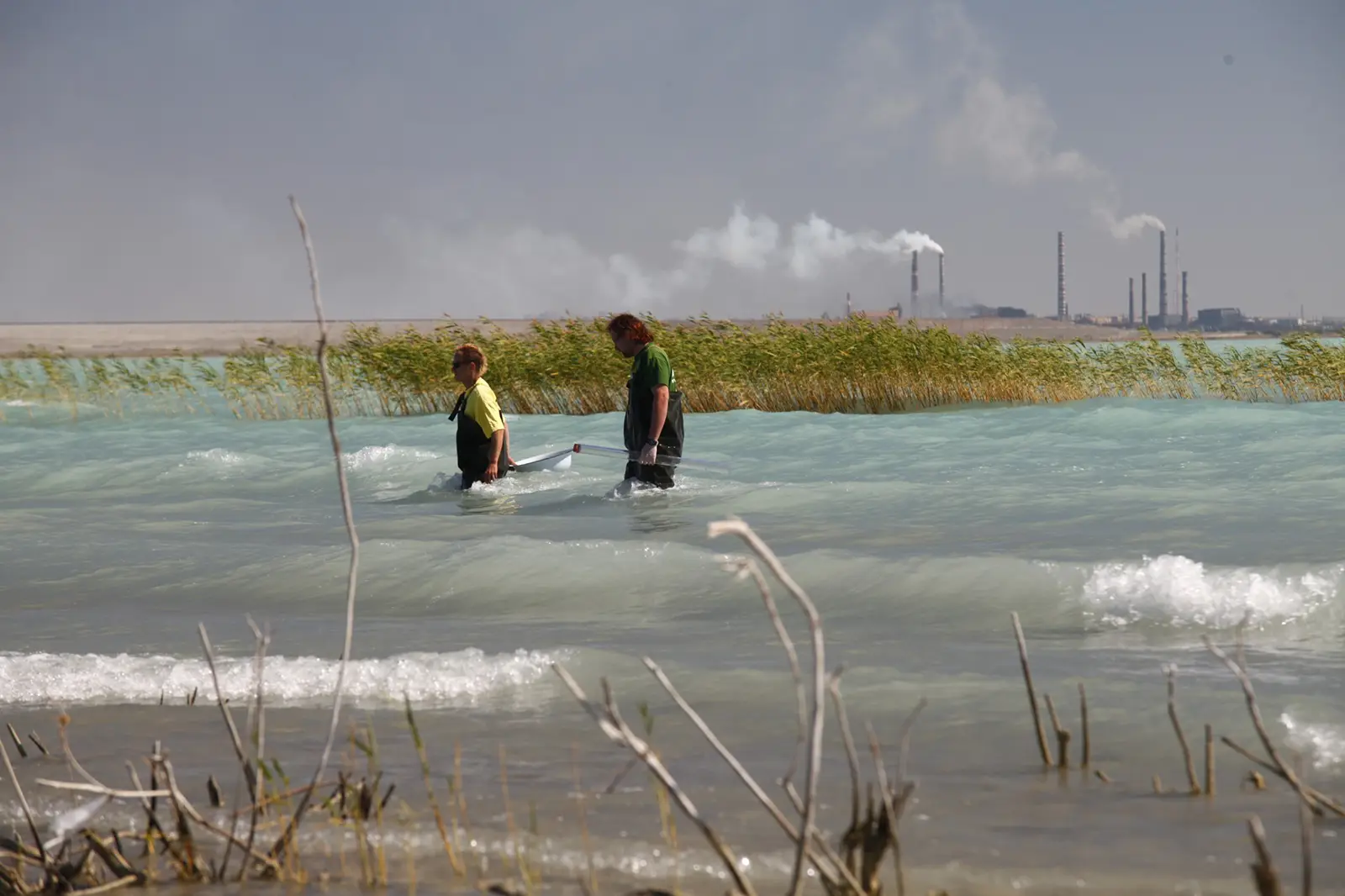 Men walking in lake Balkash. Smoke stacks in the background.