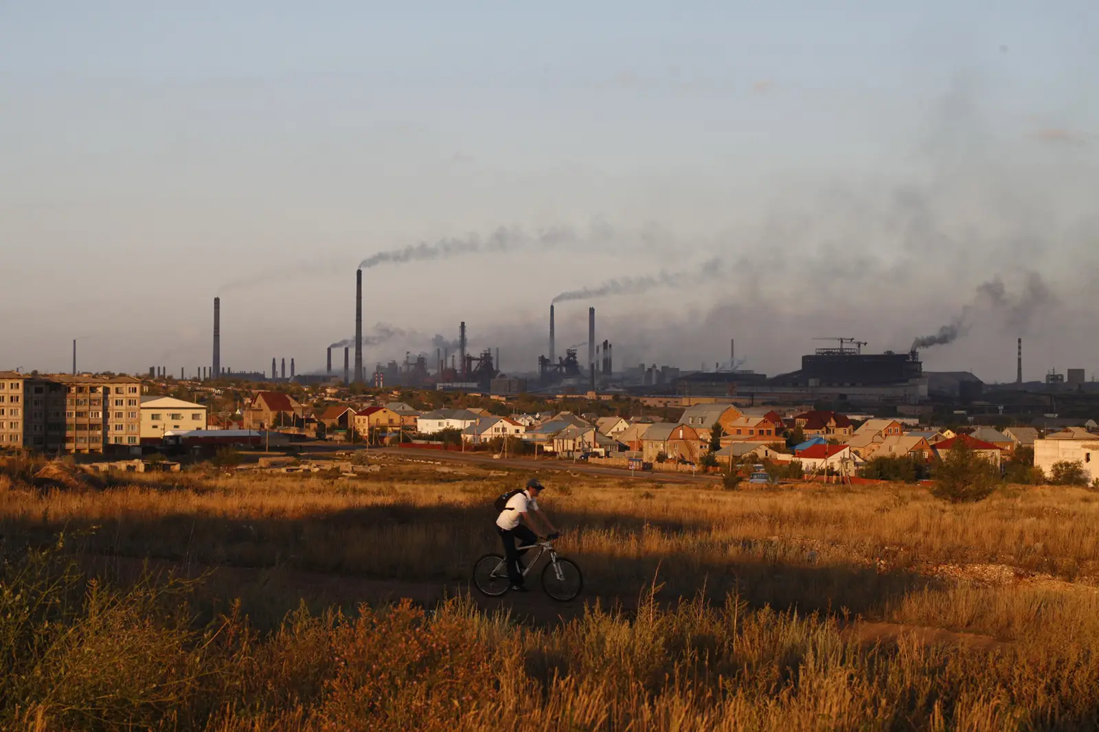 Man on a bicycle with smoke stacks in the background